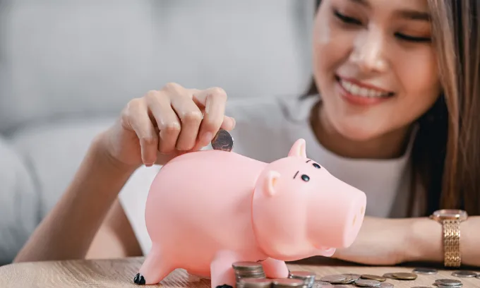 Smiling lady puts money into a piggybank