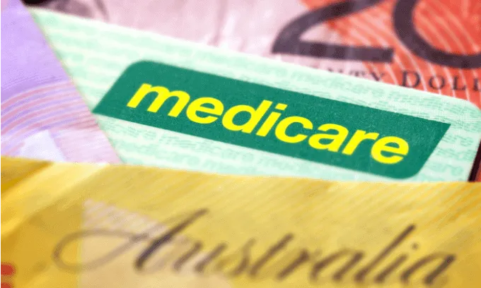 A green Medicare card sits between a fifty and twenty Australian dollar note