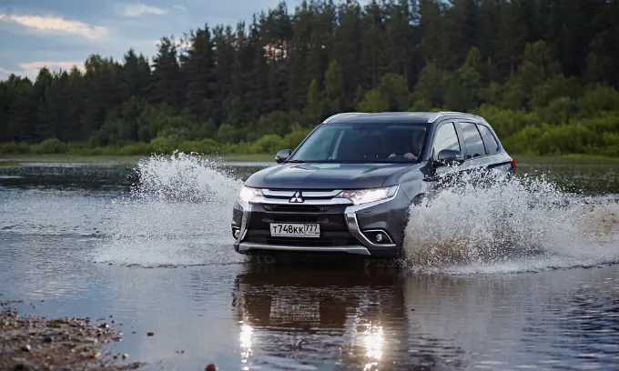 Mitsubishi Outlander driving through a shallow body of water with forestry in the background