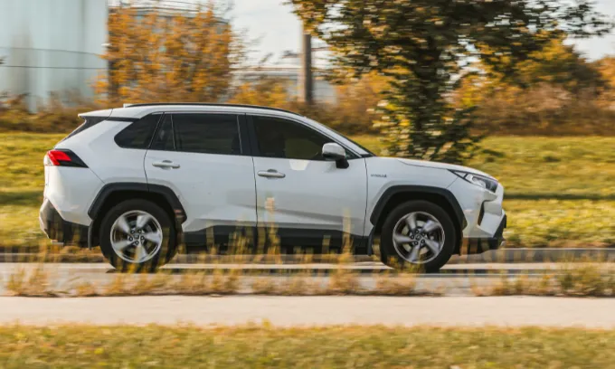 Toyota Rav4 driving in front of greenery with something industrial in the background